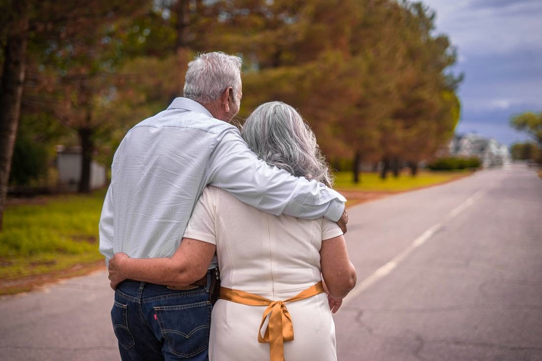 An older couple walking arm in arm down a country road